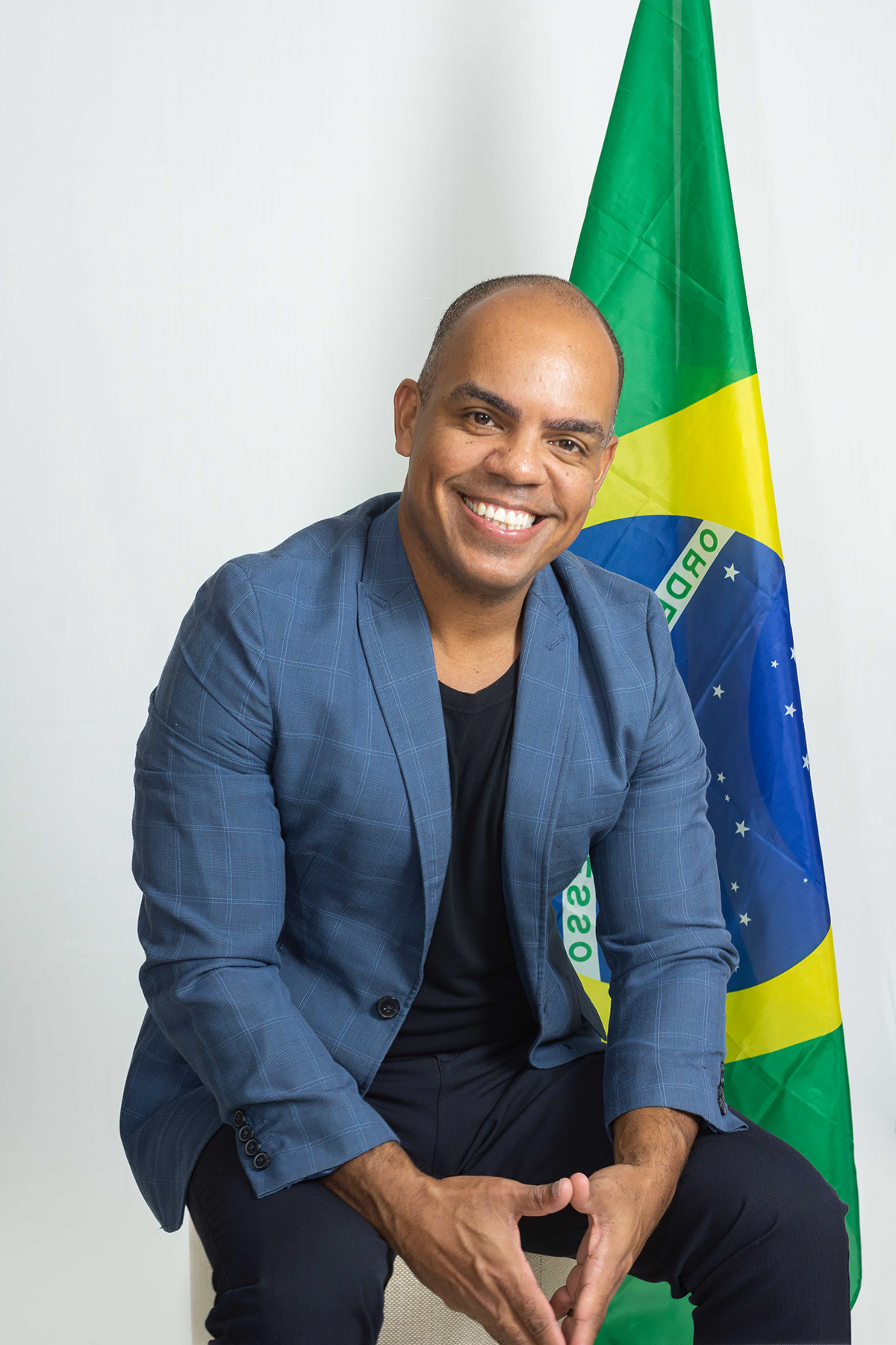 Roberto Alves Júnior de terno azul ao lado da bandeira do Brasil