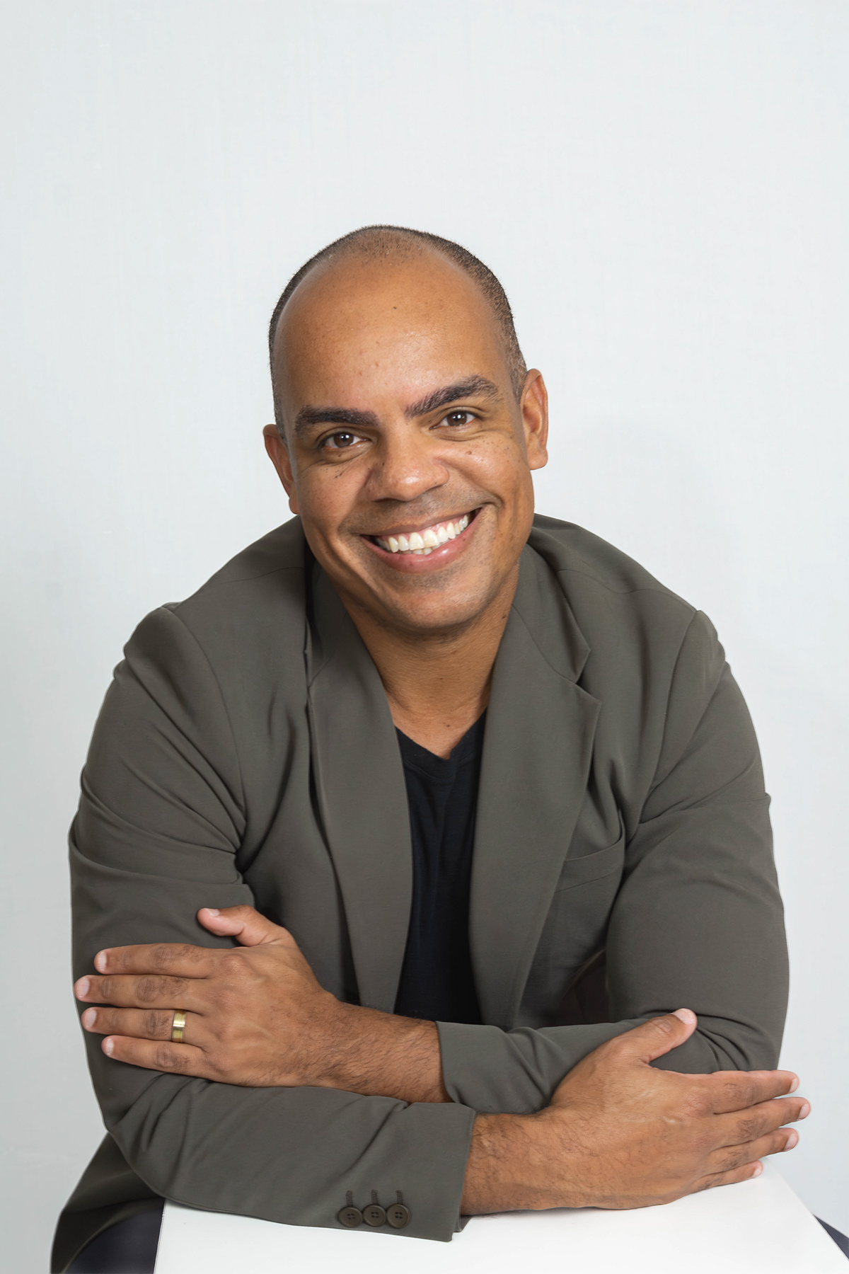 Roberto de terno marrom, sorrindo, braços cruzados